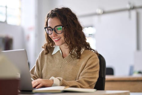 Young, happy woman at a desk using a laptop, exemplifying employee recognition