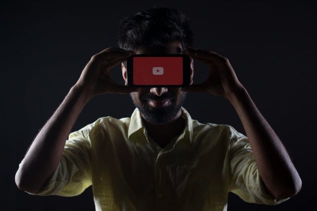 Man holding a phone with the YouTube logo at face level in a dark setting