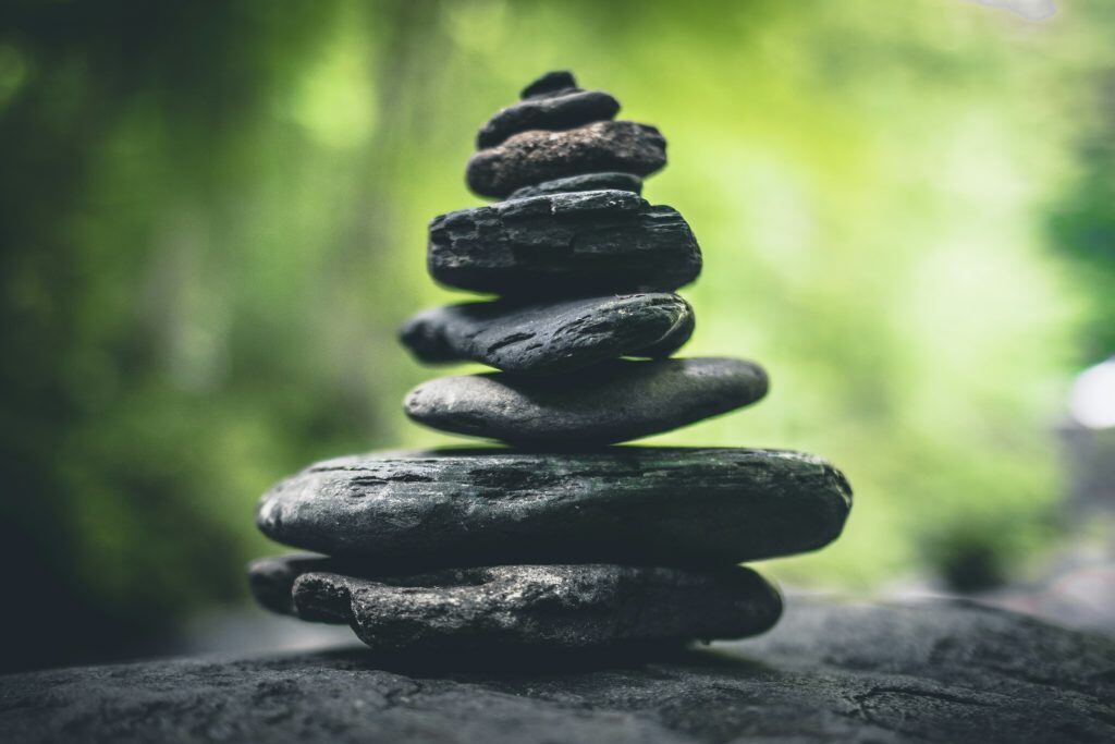 Stack of smooth black stones balanced outdoors with a blurred green background.