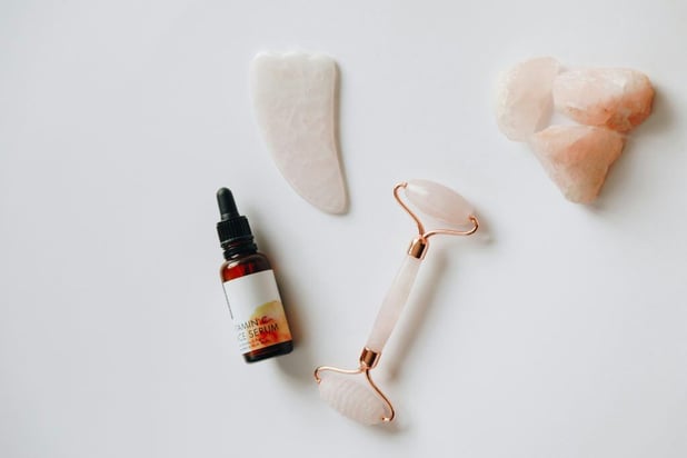 Flat lay of skincare tools: a facial roller, gua sha stone, vitamin C serum bottle, and rose quartz crystals.