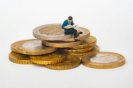 man reading a book sitting on a stack of coins