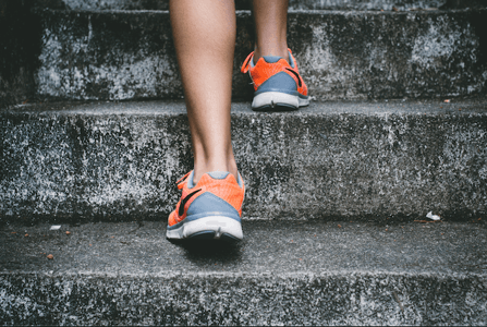 person wearing orange and grey running shoes on concrete steps