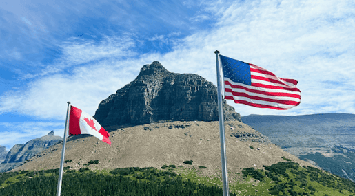 two-american-and-canadian-flags-flying-in-front-of-a-mountain